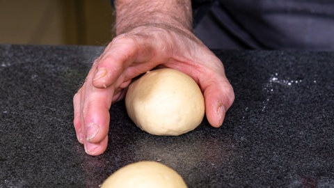 Der Hefeteig für die Dampfnudeln wird, wie im Rezept beschrieben, zu kleinen Kugeln geformt. Nach dem Backen werden die Dampfnudeln mit Vanillesauce serviert.