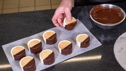 Die abgekühlten Eistaler aus Keksen und Parfait werden zur Hälfe in flüssige Schokolade getaucht.