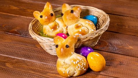 Rezept zum Backen für Ostern: Osterhase aus Hefeteig liegt in einem Osternest mit bunten Eiern.