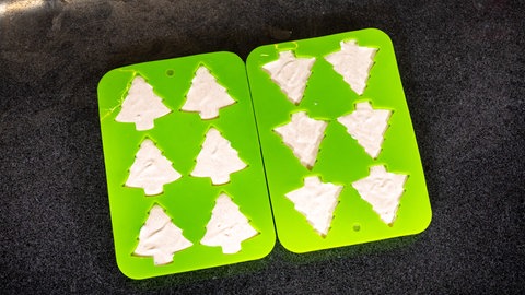Zwei grüne Formen mit je sechs Tannenbaumausbuchtungen befüllt einer hellen Creme, dem Lebkuchenparfait - das Ganze vor dunklem Hintergrund. Der Nachtisch ist fast fertig. 
