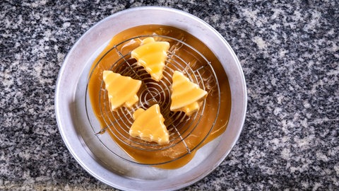 Vier Tannenbaumeis - das Lebkuchenparfait - mit hellbrauner Soße überzogen liegen auf einem Abtropfgitter, das auf einer Abtropfschale steht