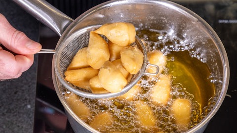Mit einem kleinen Sieb werden die in Form gestochenen und ausgebackenen Mutzenmandeln aus einem Topf mit heißem Fett gehoben.