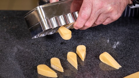 Aus einem Mutzenmandel-Ausstecher werden Mutzenmandeln in Form von Tröpfchen mit dem Finger rausgedrückt.