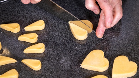 Die Mutzenmandeln wurden mit einer Herzausstecher aus dem Teig ausgestochen und eine Hand halbiert die Teigherzen zu der typischen Form.