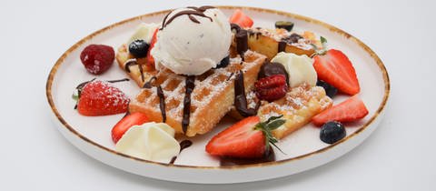 Belgische Waffeln mit Beeren und Eiscreme auf einem Teller angerichtet. Belgische Waffeln sind dicke Waffeln mit tiefem Muster und viel Platz für Toppings wie Beeren, Puderzucker oder Eiscreme. SWR1 Pfännle-Koch Eberhard Braun hat das Rezept für euch.