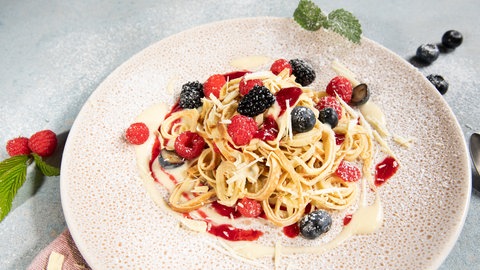 Auf einem Teller sind Flädle angerichtet als süße Variante mit Beeren, Vanillesauce und weißer Schokolade.