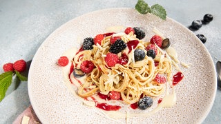 Auf einem Teller sind Flädle angerichtet als süße Variante mit Beeren, Vanillesauce und weißer Schokolade.