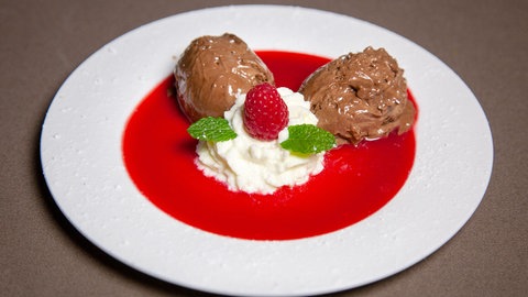 zwei Bollen mousse au chocolat mit Sahne auf Himbeersauce