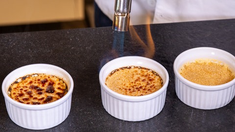 Die fertigen Crème Brûlée werden mit einem Brenner flambiert, damit der Zucker karamellisiert.