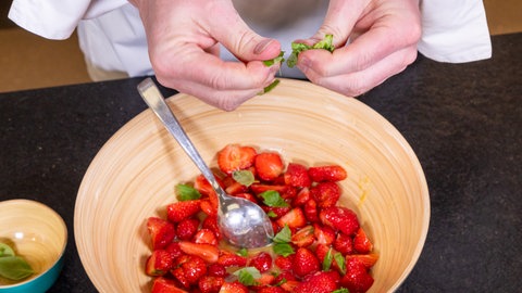 Klein geschnittene Erdbeeren in einer Schüssel werden mit Basilikum verfeinert.