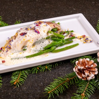 Rezept für Forellenfilet geräuchert als Vorspeise: Die Forellenfilets sind auf einem weißen Teller mit grünen Bohnen und Meerretichsoße angerichtet und mit Tannenzweigen dekoriert.