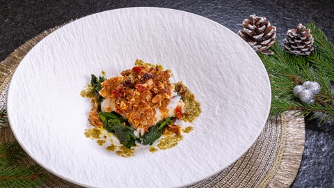 Fisch in Mandelkruste mit Spinat: Die Vorspeise vom Weihnachtsmenü in einem Teller festlich angerichtet.