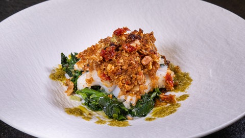 Fisch in Mandelkruste mit Spinat: Die Vorspeise vom Weihnachtsmenü schön angerichtet in einem weißen Teller.