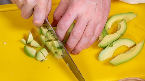 Avocado wird auf einem gelben Schneidebrett klein geschnitten.