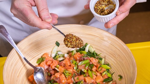 Lachstatar wird in einer Schüssel mit einer Mischung aus Senf, Essig und Zitrone gewürzt.