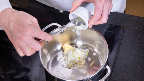 In einem Topf wird Butter mit gewürfelten Zwiebeln für eine helle Sauce für Kabeljau und Reis erhitzt. 