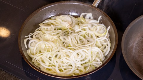 Zwiebelringe in einer Pfanne, die für den saftigen und zarten Zwiebelrostbraten in Butterschmalz angebraten werden.