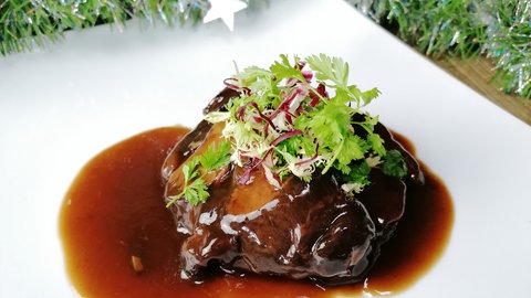 weißer Teller mit Weihnachtsdeko drumherum mit einem Stück Schmorbraten mit Soße und Kräutern obenauf
