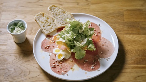 Carpaccio vom Jungbullen mit Wachtelei im Salatnest auf einer Holzplatte