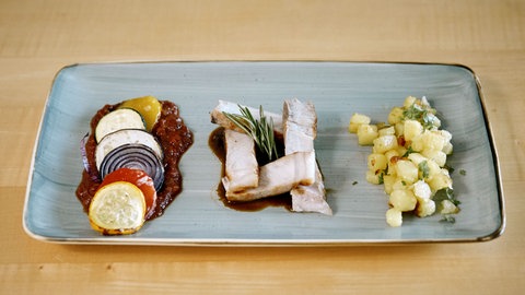 Dry Aged Kotelett vom Sattelschwein mit Ratatouille und Kartoffelwürfeln auf einem Teller