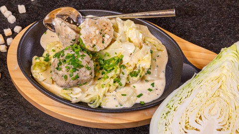 Die Knödel mit Pfälzer Leberwurst sind in einer dunklen Pfanne mit Filderkrautfleckerl schön angerichtet, an der Seite liegt ein halbierter Kohl.