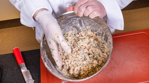 Die Masse für die Knödel mit der Pfälzer Leberwurst wird in einer Metallschüssel von eine behandschuhten Hand vermengt.