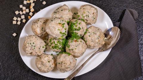 Ein weißer Teller voller Knödel mit Pfälzer Leberwurst. An der Seite des Tellers liegt ein Servierlöffel.