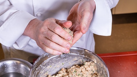 Zwei angefeuchtete Hände formen aus der Pfälzer Leberwurst Semmelbrösel Masse Knödel.