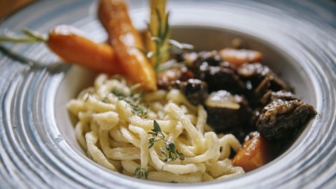 Boeuf Bourguignon mit hausgemachten Spätzle und karamellisierten Karotten auf einem Glasteller