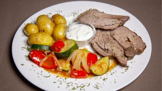 Gegrillte Lammkeule, Kartoffeln und Grillgemüse auf einem Teller