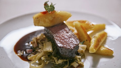 Damhirschrücken mit Schupfnudeln, Apfelspalten, Speck-Spitzkohl und Preiselbeeren auf einem Teller