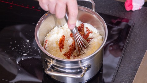 Die Sahnesauce für den Chicorée wird in einem Topf zubereitet. Zur Sahne kommen Tomaten und Käse hinzu. 