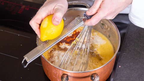Eine Zitrone wird mit einer Reibe über dem Topf mit der heißen Suppe gerieben.