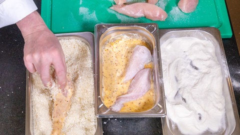 Eine Panierstation für das Backhendl: Drei Schalen mit Ei, Mehl und Bröseln in denen das Hühnchenfleisch gewendet wird.