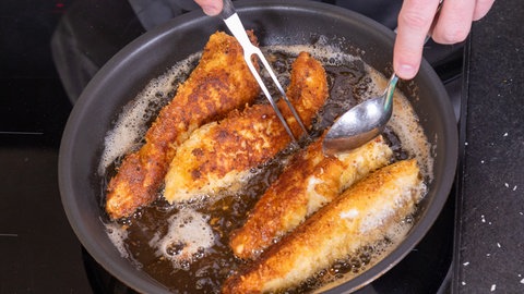 Das Hühnchenfleisch für das Backhendl wird in einer Pfanne gebraten.