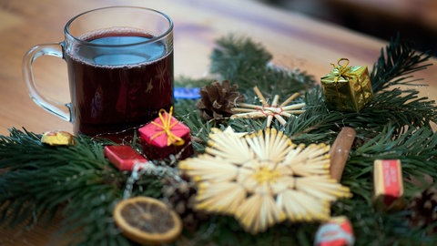 Ein Glas roter Glühwein steht neben einem Weihnachtsgesteck.