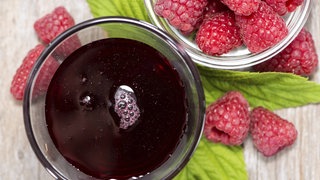 Frische Himbeeren und ein Glas mit Himbeersirup