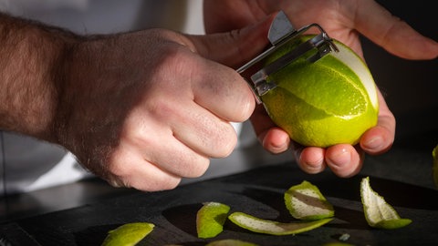 Limettenschalen werden mit einem Sparschäler in dünne Streifen geschnitten