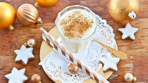Ein Glas Eierpunsch mit Zimt, Plätzchen und Weihnachtsdeko.