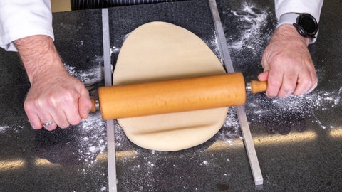 Mit einem Nudelholz wird, wie im Rezept beschrieben, der Hefeteig für die Herzen ausgerollt.