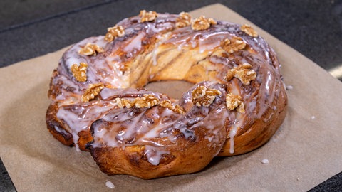 Auf einem Backpapier liegt ein frischer Hefekranz, der aus einem Hefezopf geformt wurde. Die Füllung ist aus Marzipan und Walnuss.