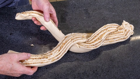 Bevor es ein Hefekranz wird, muss ein Hefezopf geflochten worden. Gefüllt ist der Hefeteig mit Marzipan und Walnuss.