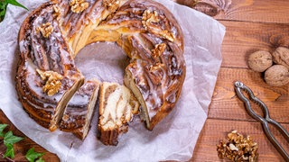 Eine saftiger Hefekranz, der aus einem Hefezopf geformt wurde, liegt auf einem Backpapier. Gefüllt ist der Kranz mit Marzipan und Walnuss.