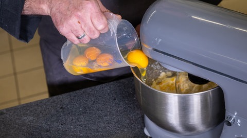 Eier werden aus einem Messbecher in eine Küchenmaschine gegeben.