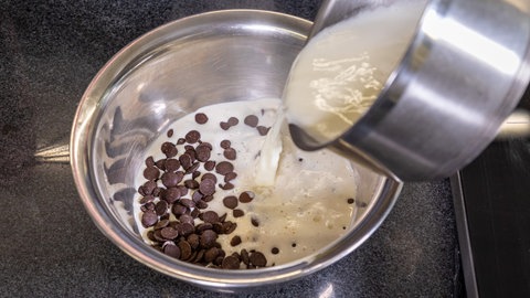 Für den Schokokuchen wird eine heiße Mischung von Sahne und Milch mit der gehackten Kuvertüre glattgerührt.