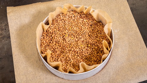 Hülsenfrüchte wie Erbsen und Linsen helfen, dass beim Vorbacken des Bodens für den Schokokuchen der Mürbeteig nicht absenkt.