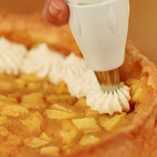 Eine Frau sprüht Sahnehäubchen auf einen Apfelkuchen