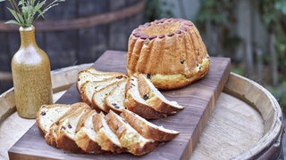 Ein geschnittener und ein ganzer Gugelhupf auf einer Holplatte auf einem Holzfass