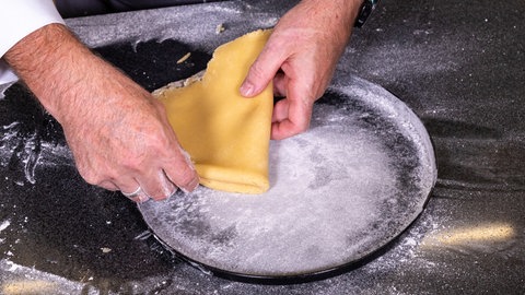 Rezept für Apfelwähe: Der Mürbeteig für den Apfelkuchen wird ganz einfach gefaltet und dann in der Blech gelegt.