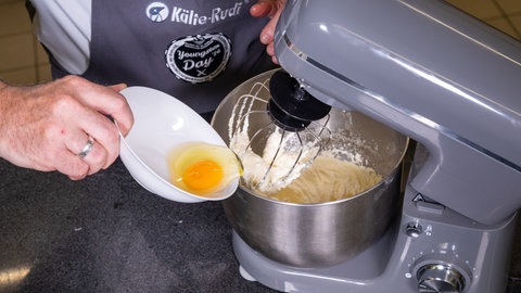 Ein Konditor gibt ein Ei in eine Teigrührmaschine.